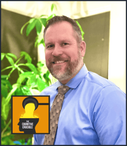 a person in a blue shirt and tie standing in front of a plant